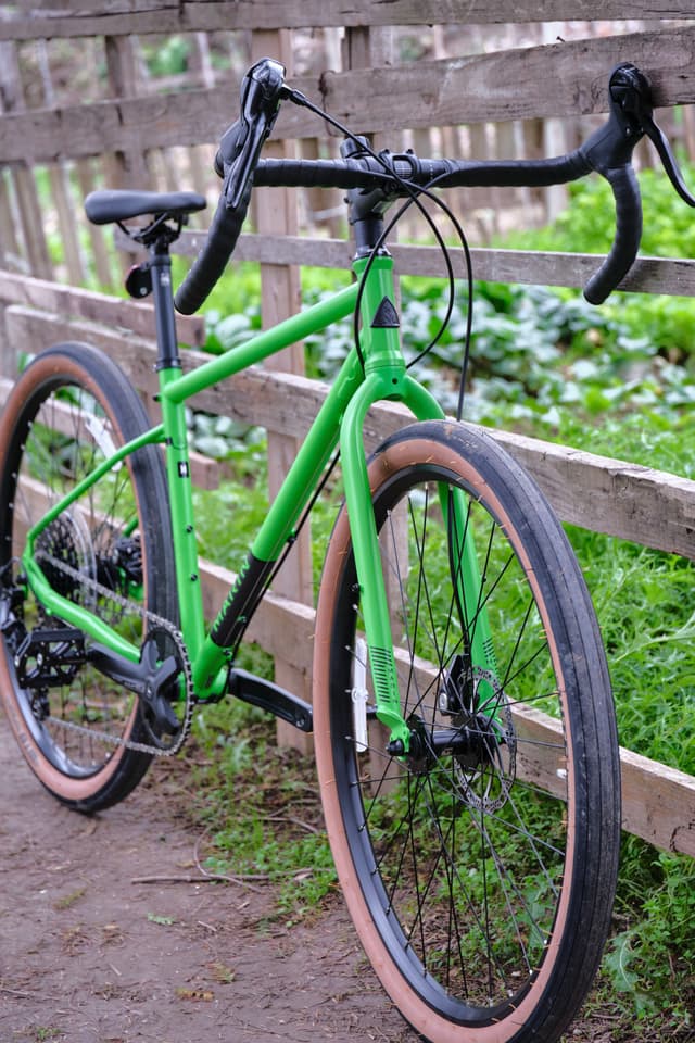 Bright green gravel bike leaning against a wooden fence