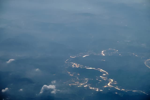 Aerial view of a wide river reflecting sunlight through a hazy, cloudy landscape